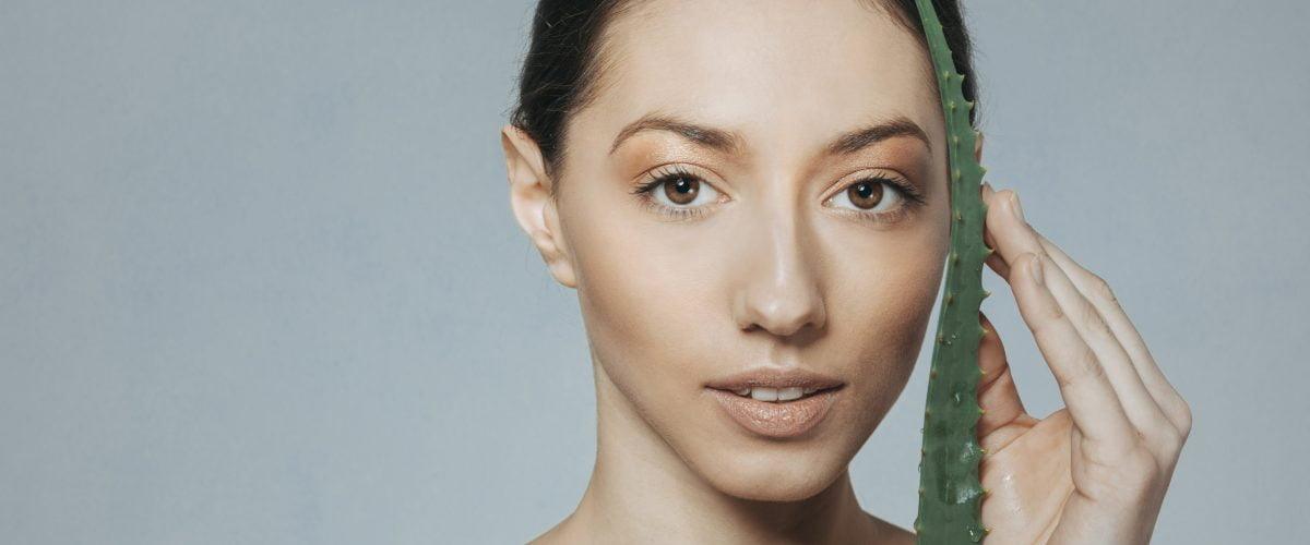 Woman holding fresh aloe vera leaf near face, promoting natural skincare benefits
