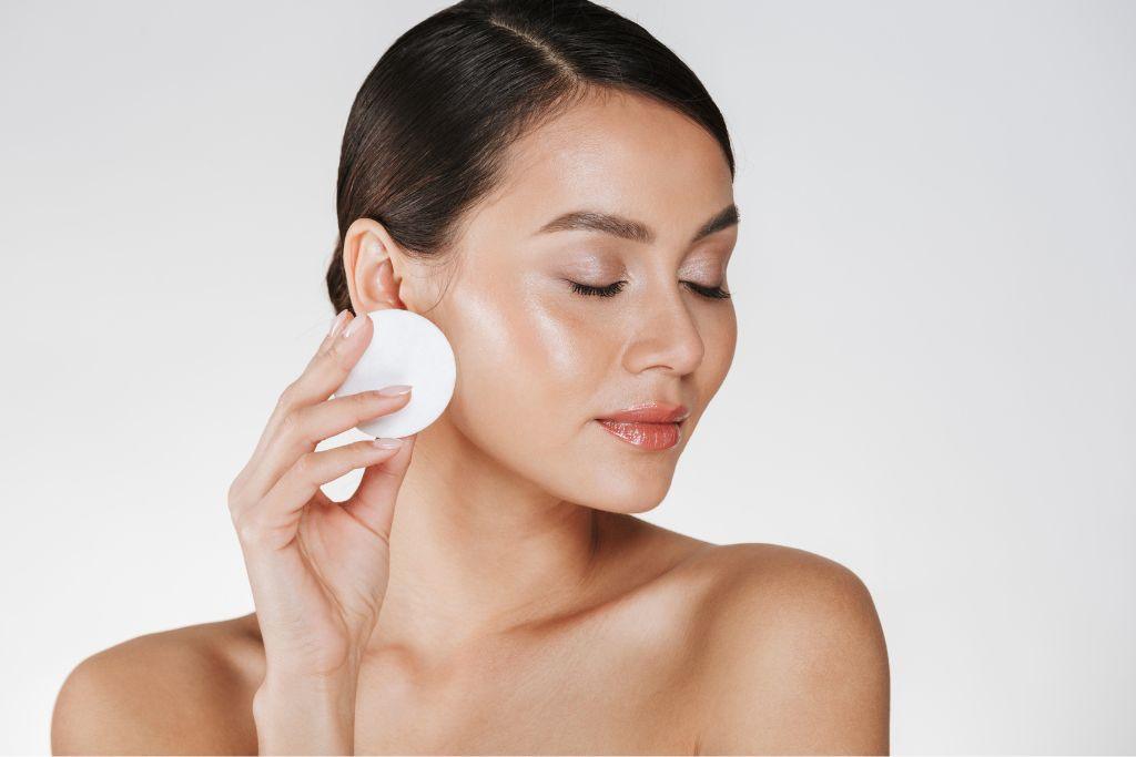 Woman applying toner to face with cotton pad, glowing skin, skincare routine