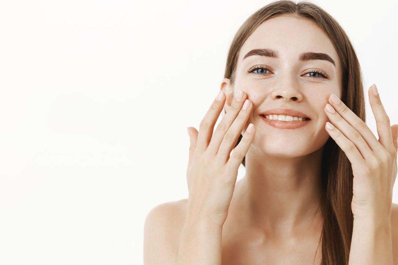 Smiling woman applying day cream to face for natural skincare on white background