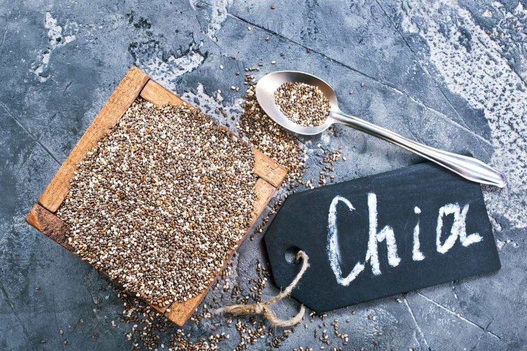 Chia seeds in a wooden box with a spoon and a black label reading 'Chia' on a gray surface