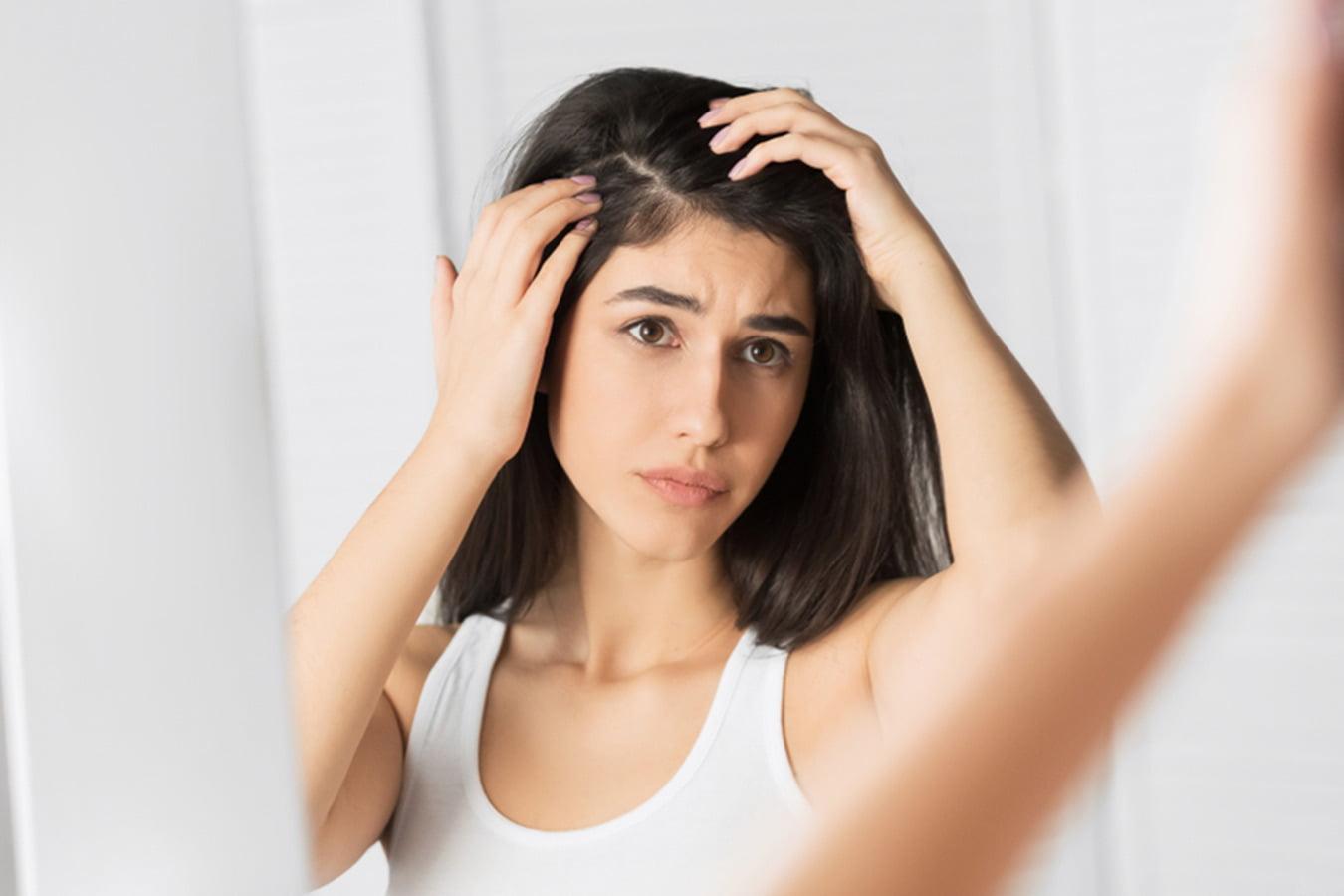 Woman examining scalp and hair for dandruff in front of mirror