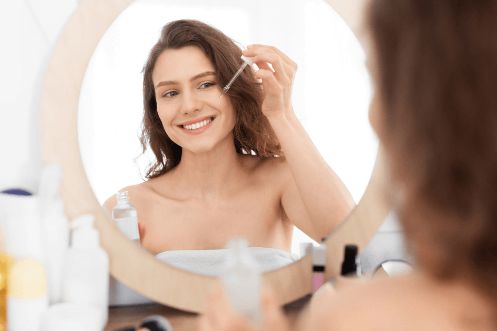 Woman applying face serum with dropper in front of mirror, skincare routine concept
