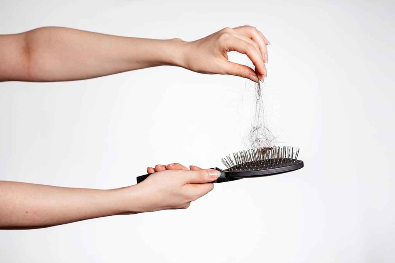Hand holding hairbrush with visible hair fall, concept of hair loss and haircare