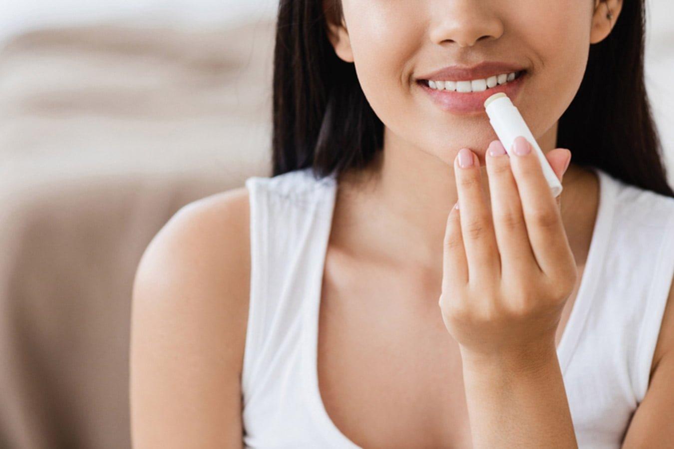 Woman applying lip balm for natural lip care, close-up in a bright indoor setting