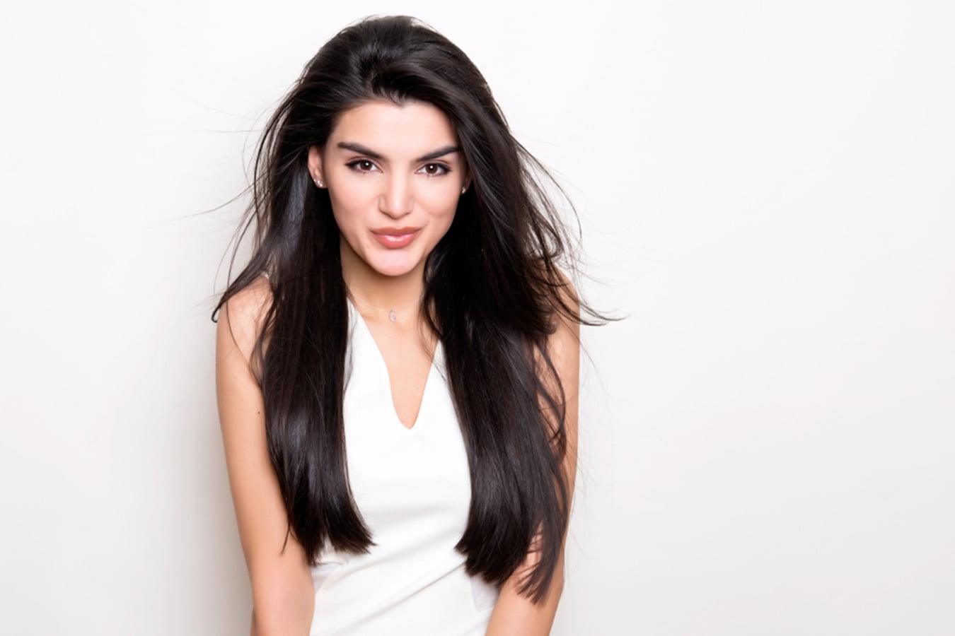 Woman with smooth, long, straight black hair and clear skin in a white top, beauty concept