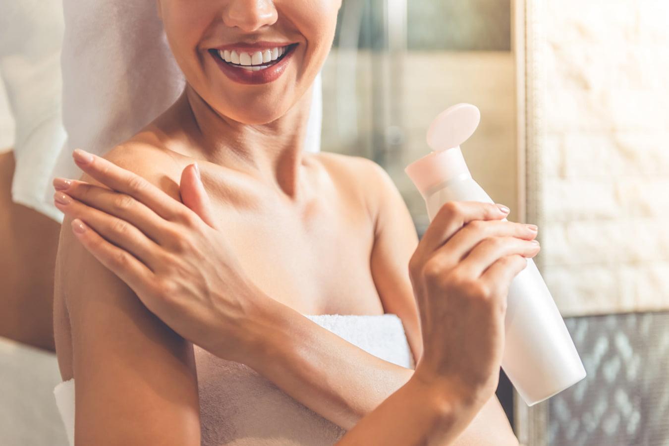 Woman applying natural body lotion on shoulder after bath in bathroom