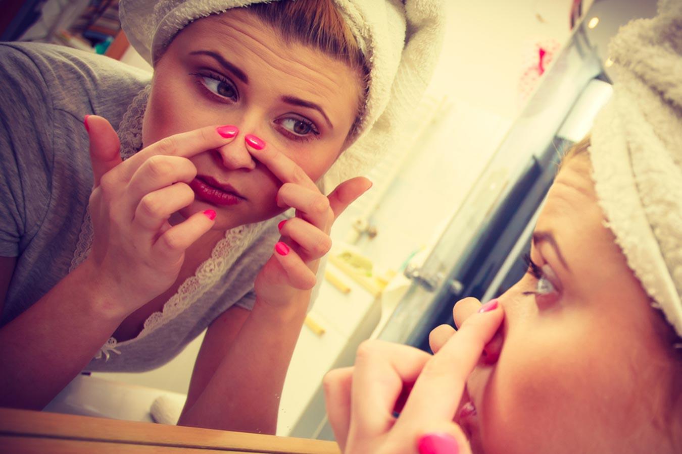 Woman with towel on head examining nose skin in bathroom mirror, skincare routine concept