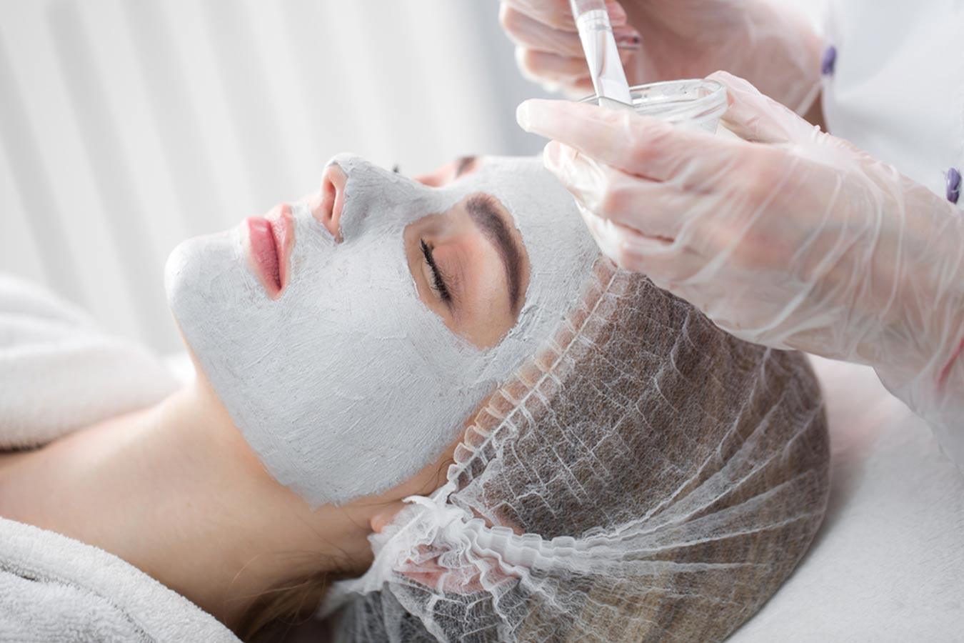 Woman receiving facial treatment with white face mask in a spa setting, beauty skincare.