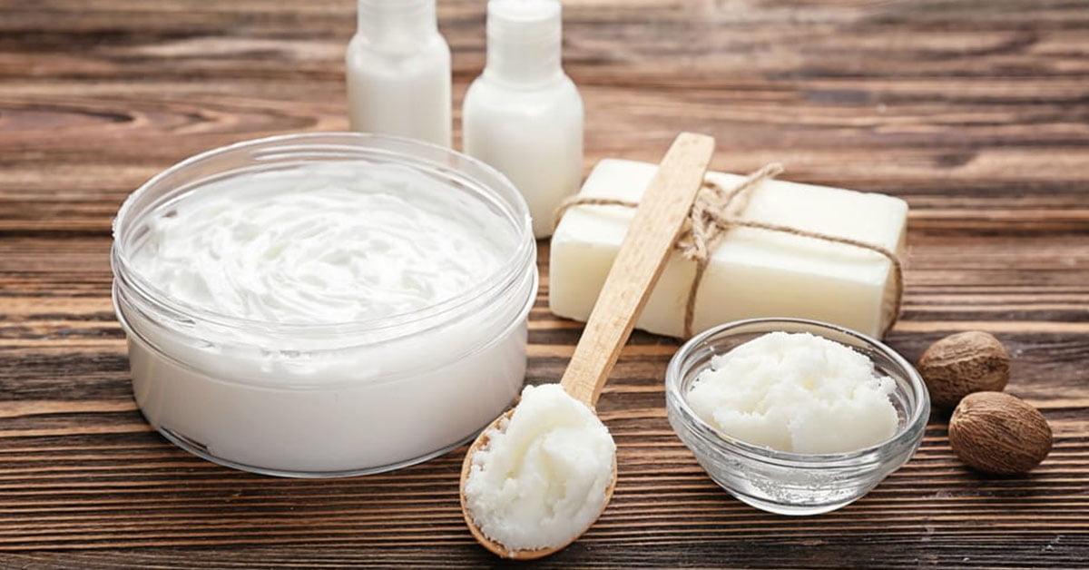 Natural skincare cream, soap bars, and glass containers on wooden table with shea nuts