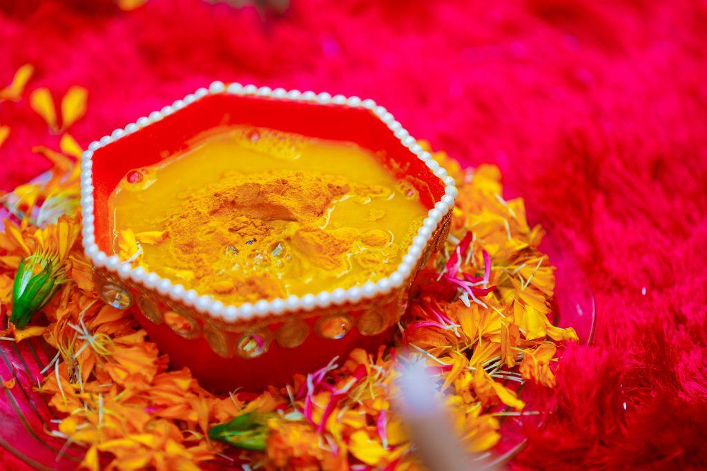 Traditional ubtan paste in a red decorative bowl surrounded by marigold petals for pre-wedding skincare.