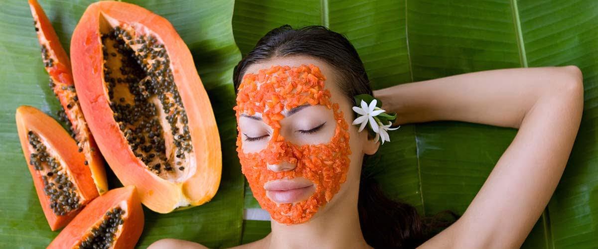 Woman relaxing with papaya face pack, surrounded by papaya slices, on green leaf background