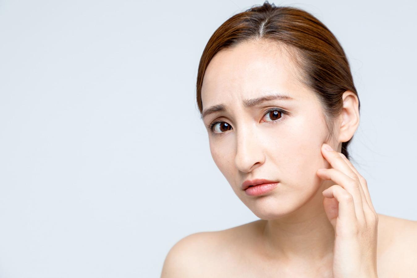 Young woman with clear skin touching face, showing concern about dry or irritated skin