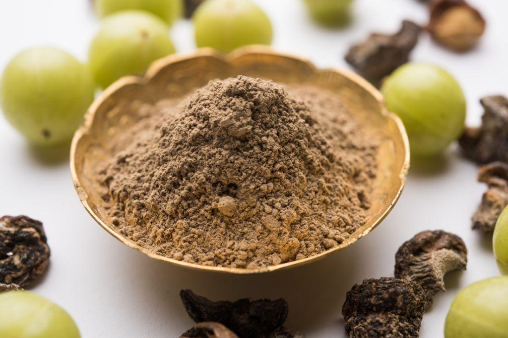 Amla powder in a brass bowl surrounded by fresh amla fruit and dried pieces, natural hair care