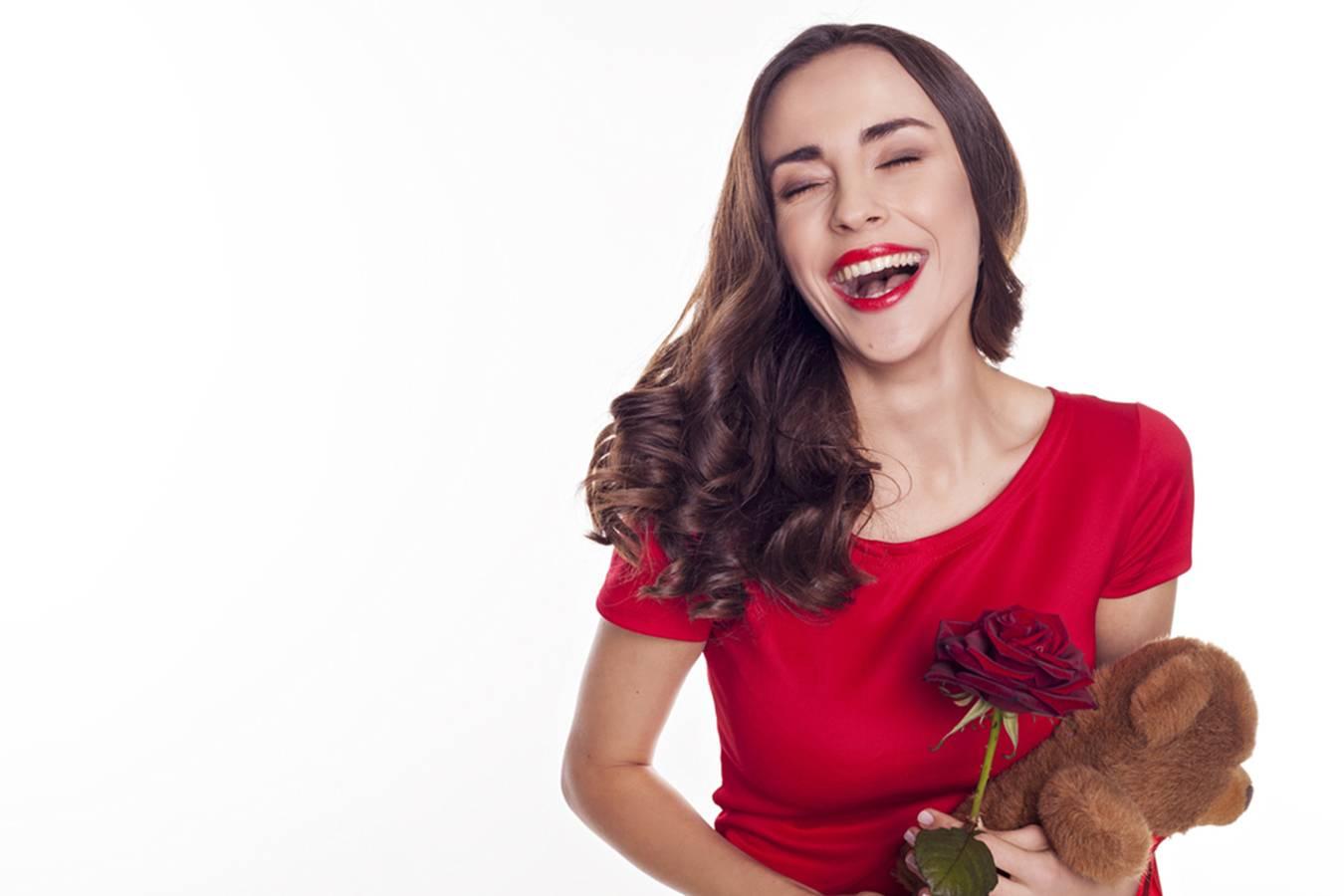 Smiling woman with clear skin in red dress holding a red rose and teddy bear, white background