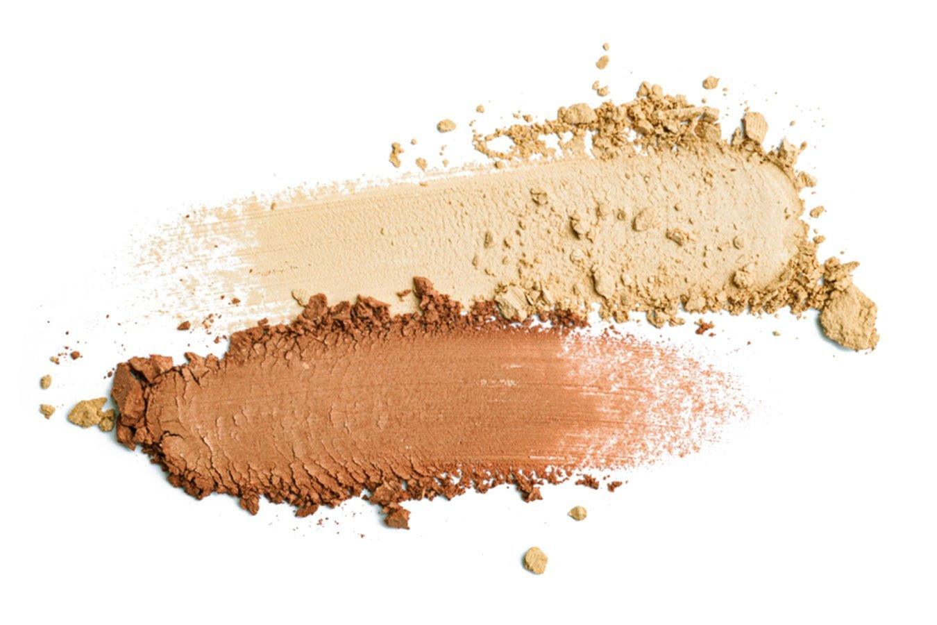 Two shades of loose blusher powder, beige and bronze, smeared on a white background
