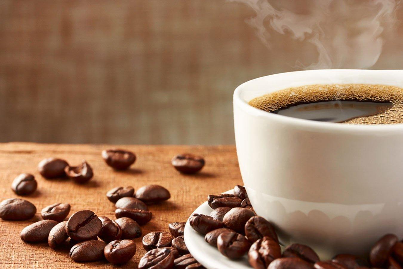 Steaming hot coffee in white cup with coffee beans on wooden table