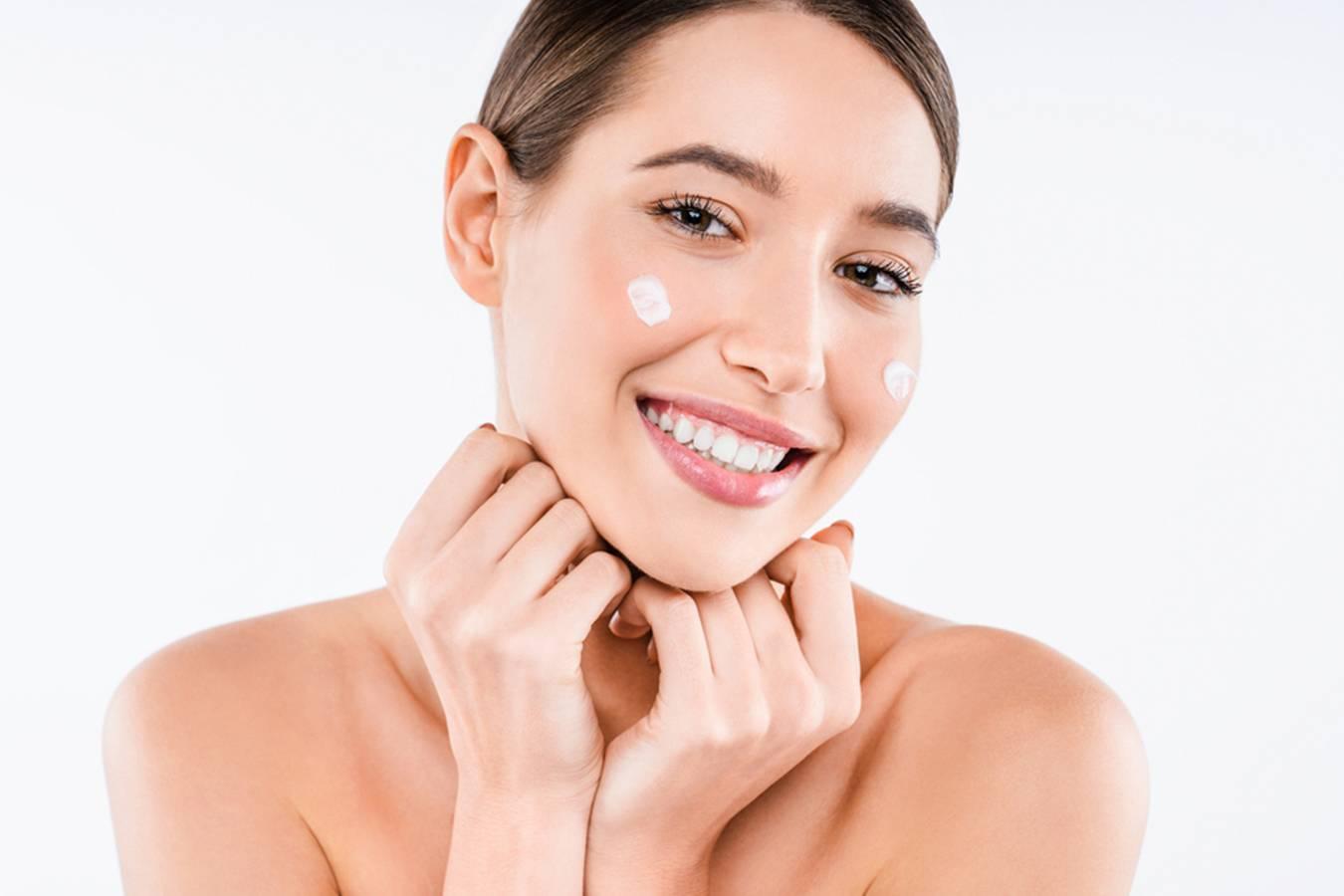 Smiling woman with glowing skin applying face cream for natural skincare