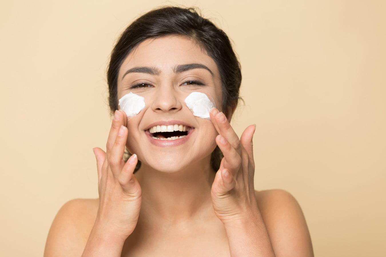 Smiling woman applying face cream to cheeks, skincare and beauty concept