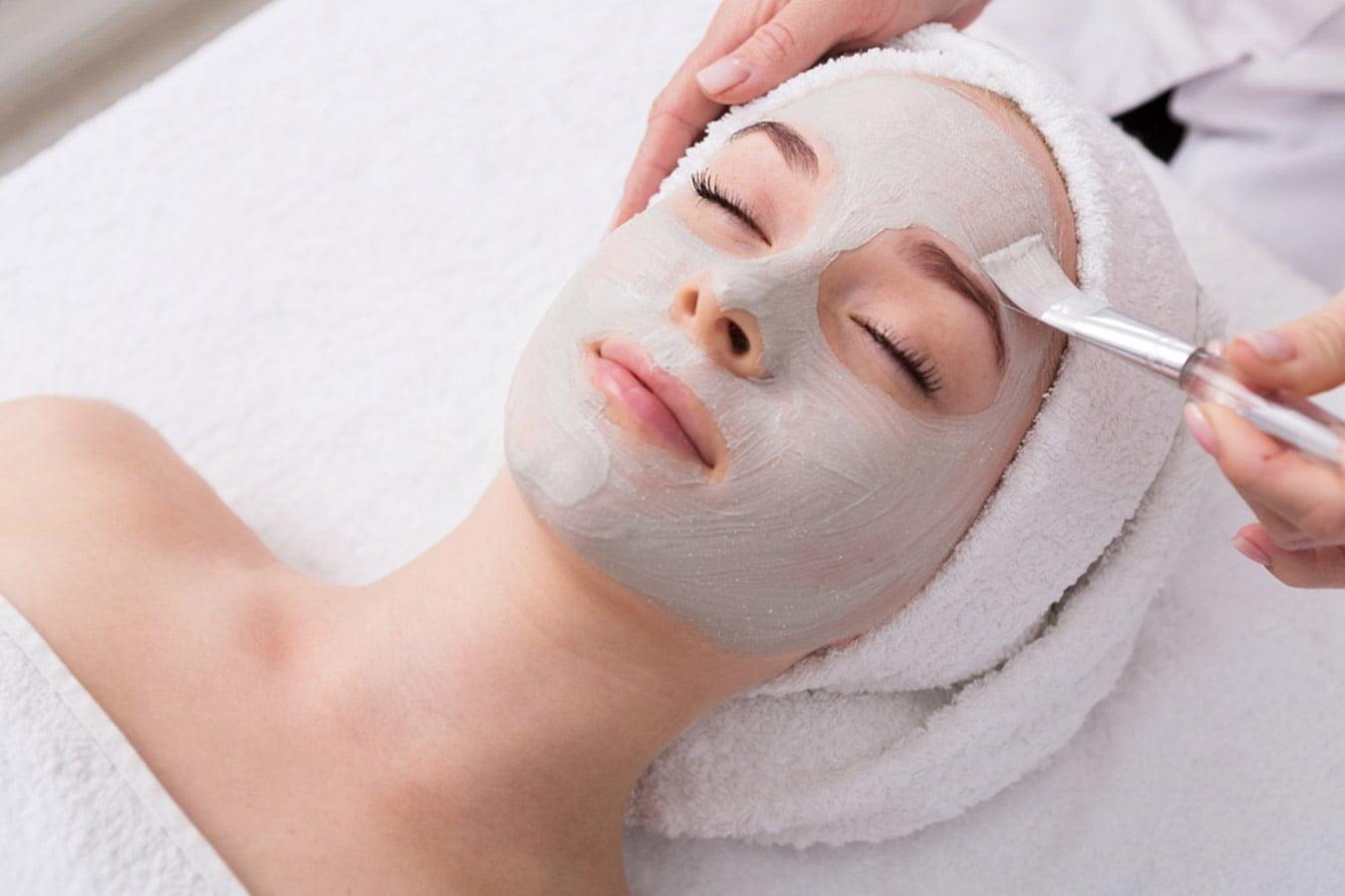 Woman receiving facial peel mask treatment at spa, relaxing with towel wrap