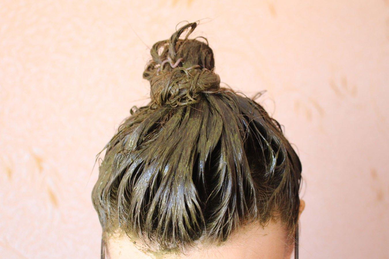 Person with hair tied in a bun, covered in herbal henna hair pack.