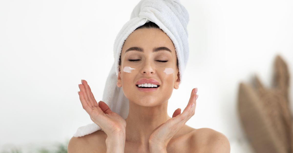 Woman with towel on head applying moisturizer to face, winter dry skin care concept