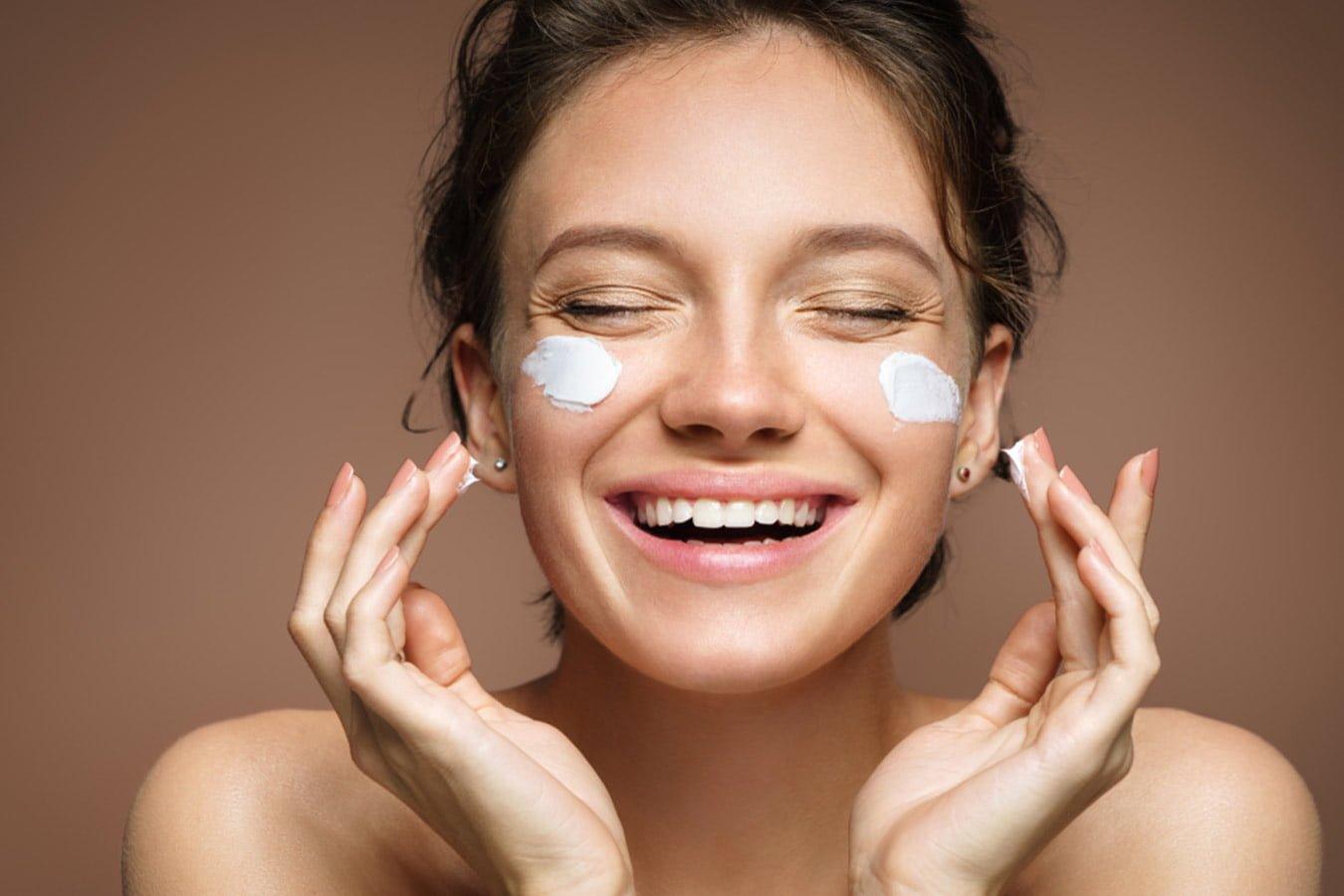Smiling woman applying moisturizing cream to her face, skincare routine concept