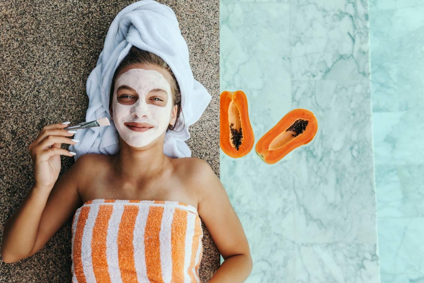 Woman applying papaya facial mask, wrapped in towel, with fresh papaya halves nearby