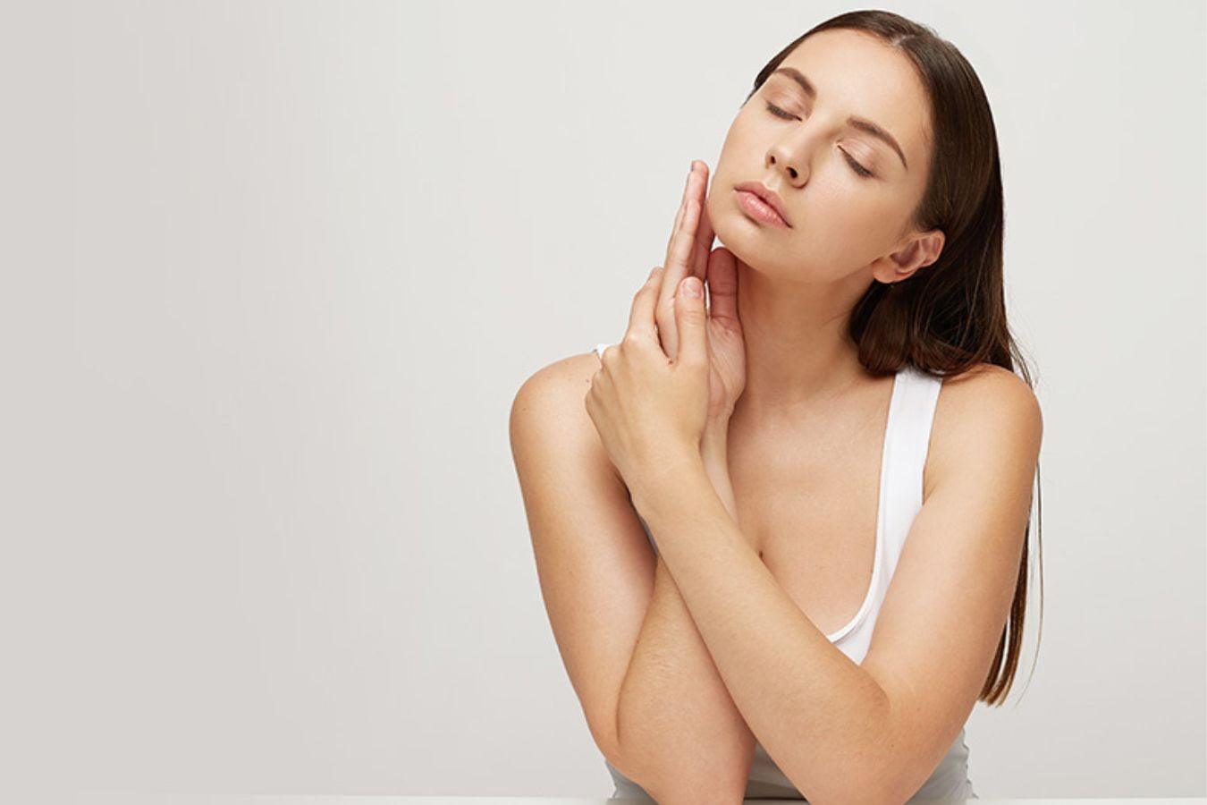 Woman with clear skin practicing night skincare routine, touching face gently in minimal setting