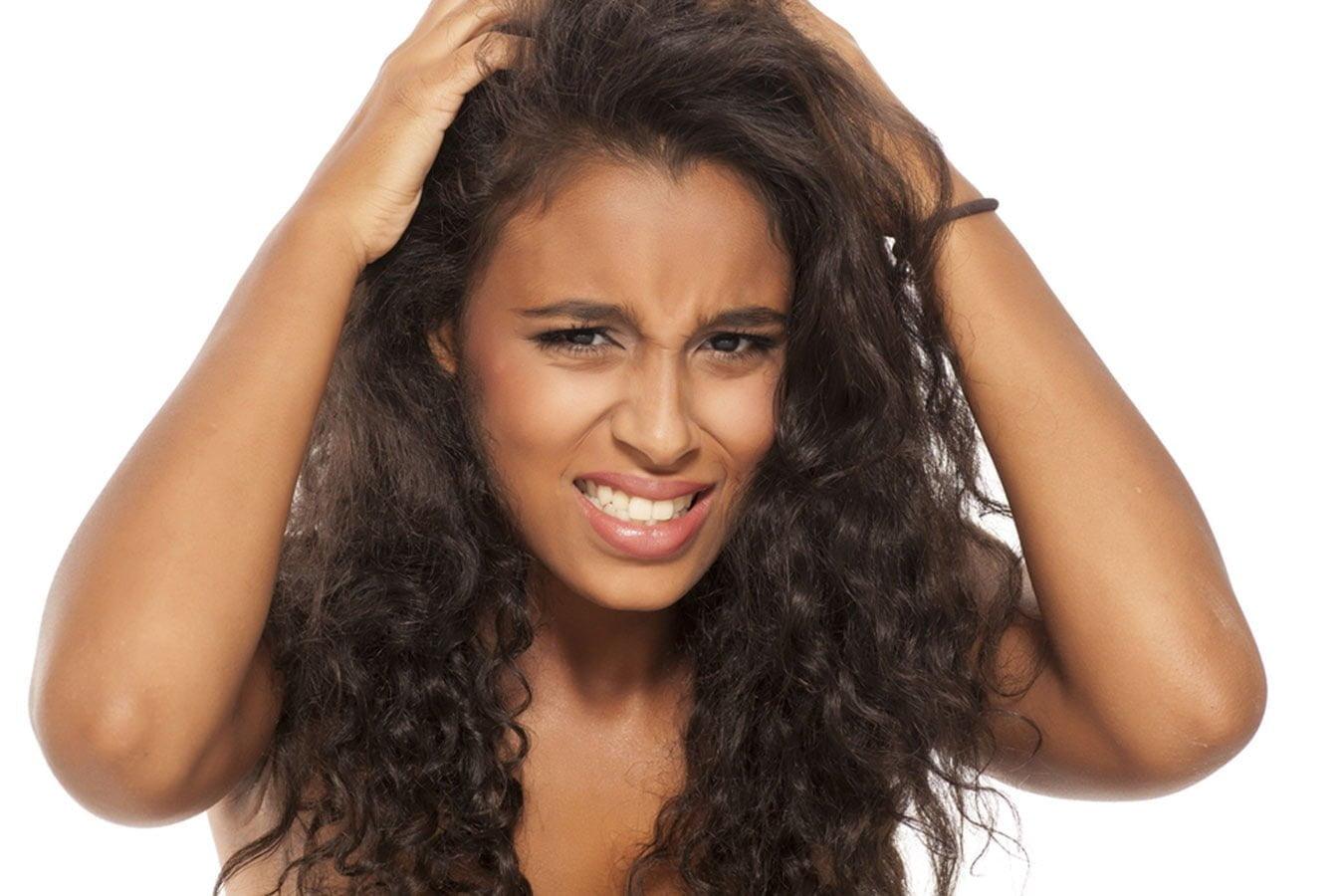 Woman with curly hair scratching itchy scalp, showing hair care concern on white background