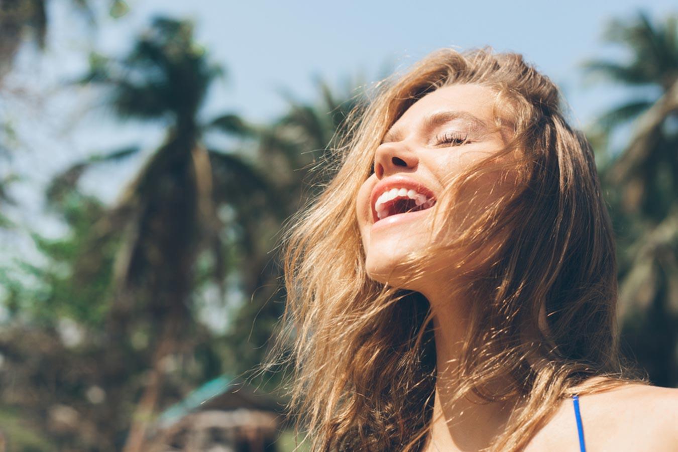 Smiling woman with healthy hair enjoying sunlight outdoors with palm trees in background