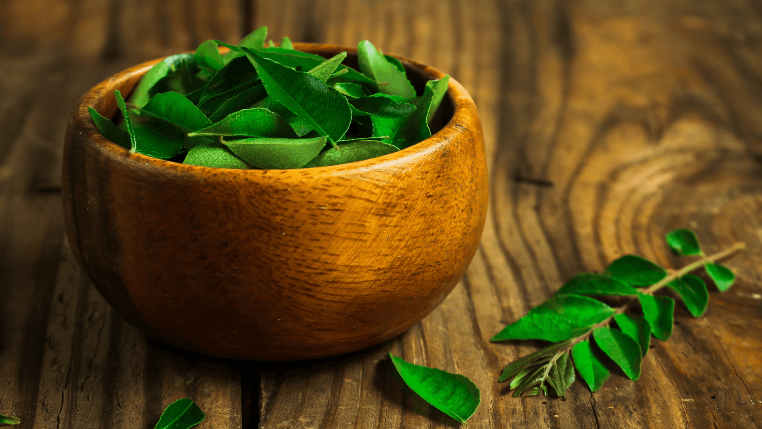 Fresh green curry leaves in a wooden bowl on rustic wooden table, herbal skincare ingredient