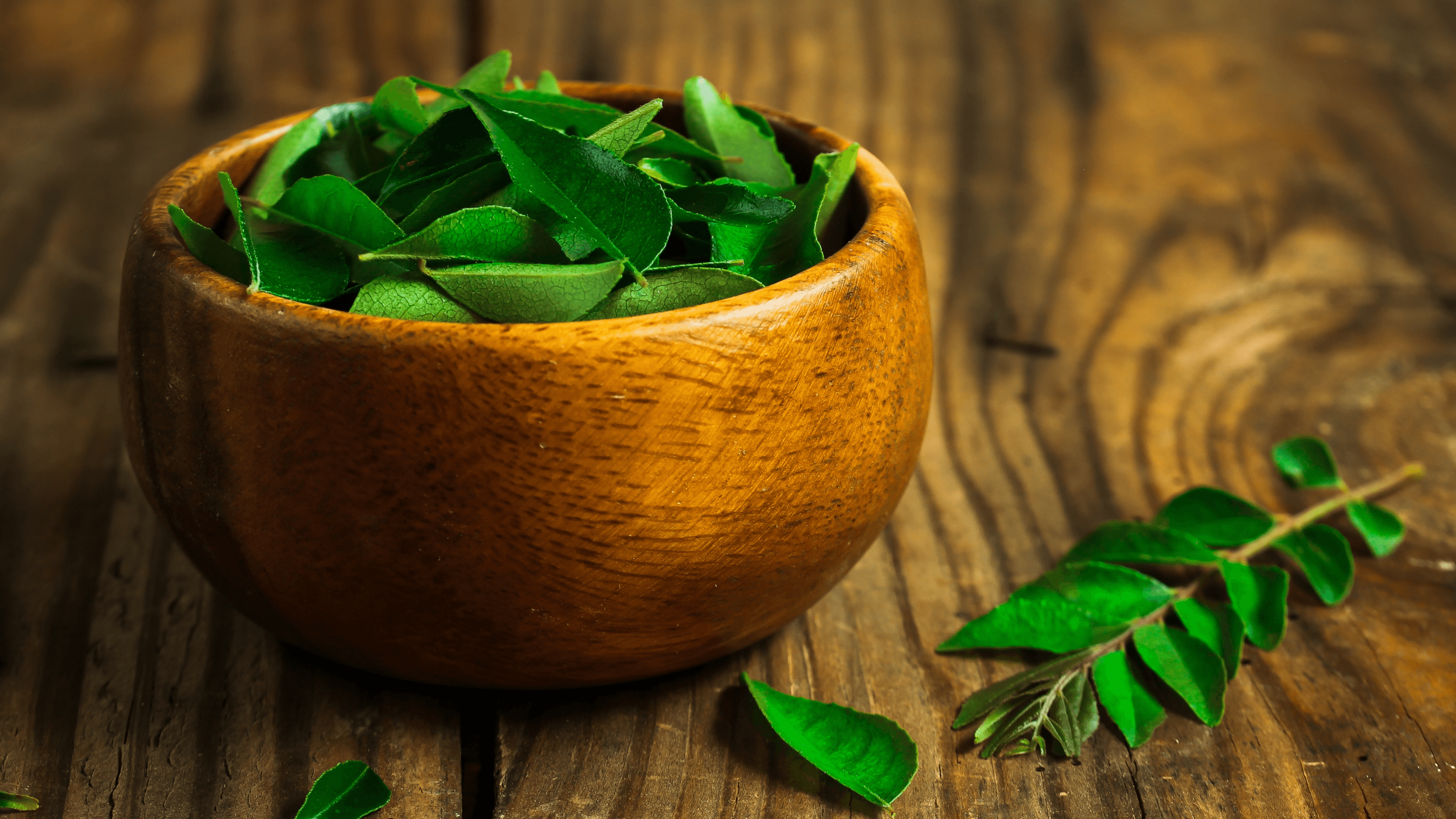 Fresh green curry leaves in a wooden bowl on rustic wooden table, herbal skincare ingredient