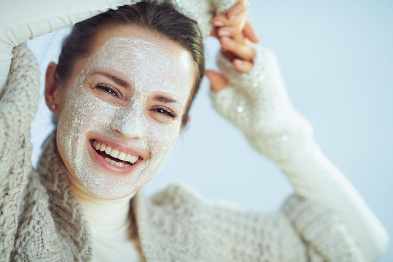 Smiling woman wearing a winter sweater with a natural face mask, winter skincare concept.