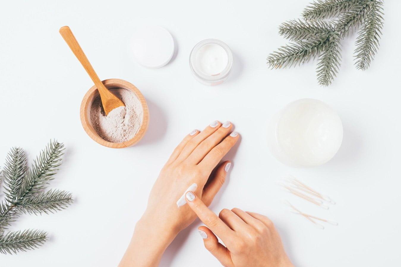 Applying moisturizing winter cream on hands with skincare ingredients and pine branches