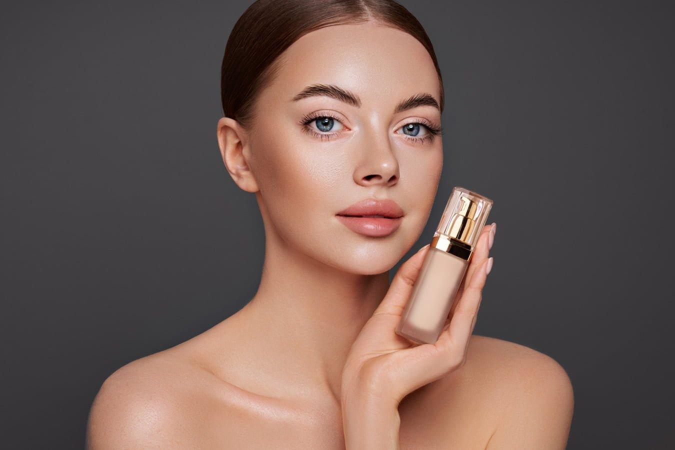 Woman with clear skin holding natural liquid foundation bottle, beauty skincare concept