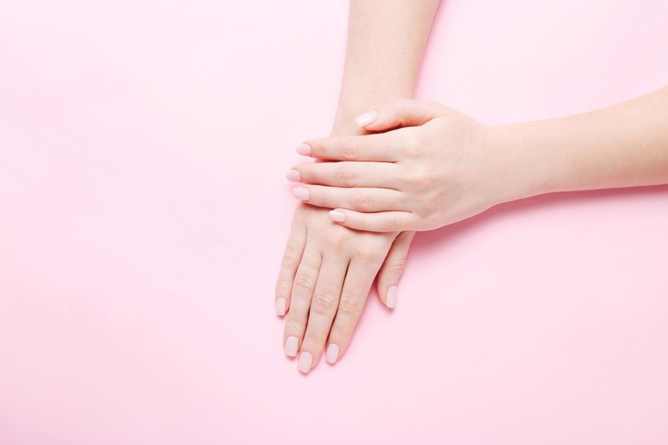 Woman's smooth hands with manicured nails on pastel pink background, skincare concept
