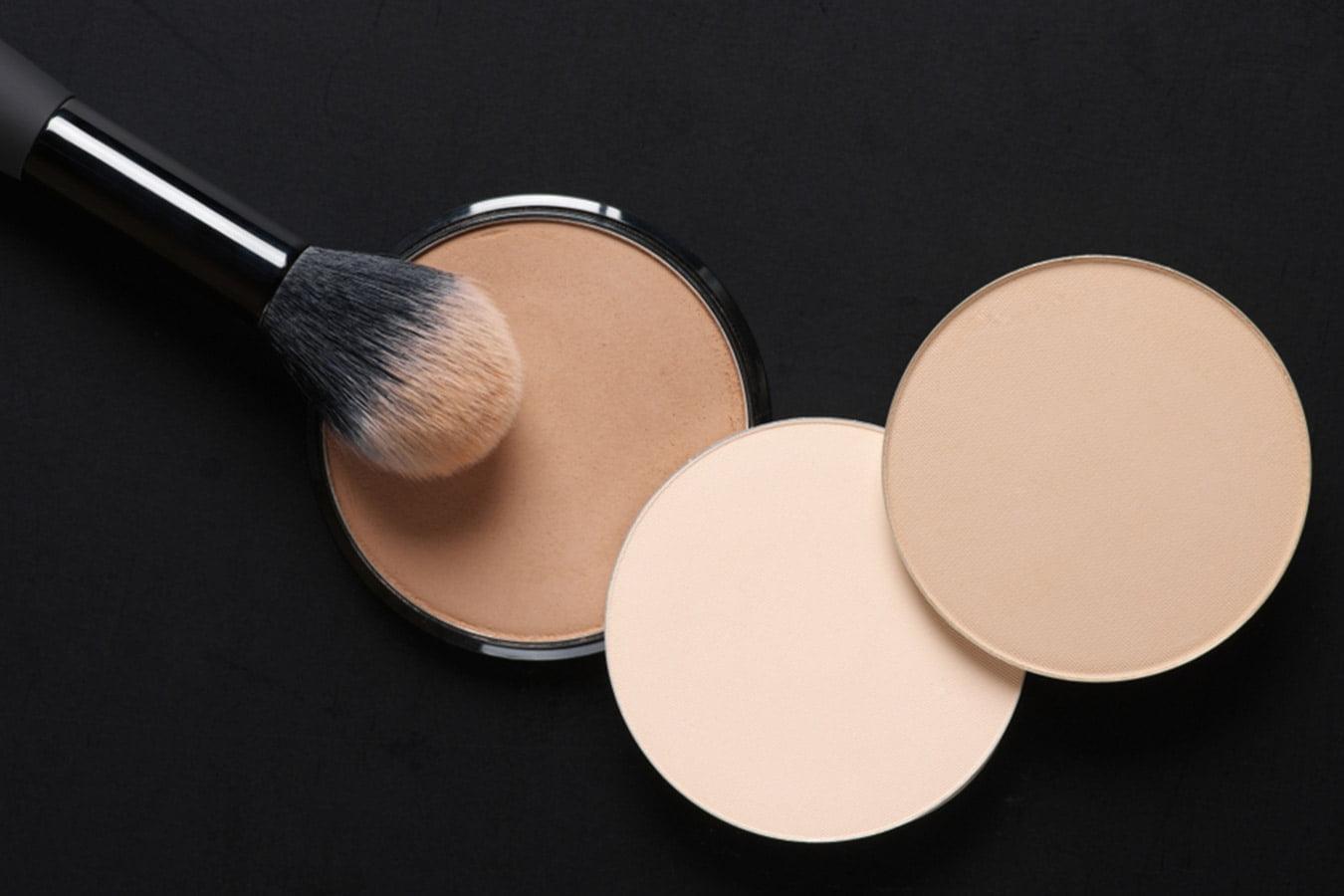Compact face powders in various shades with a makeup brush on a black background
