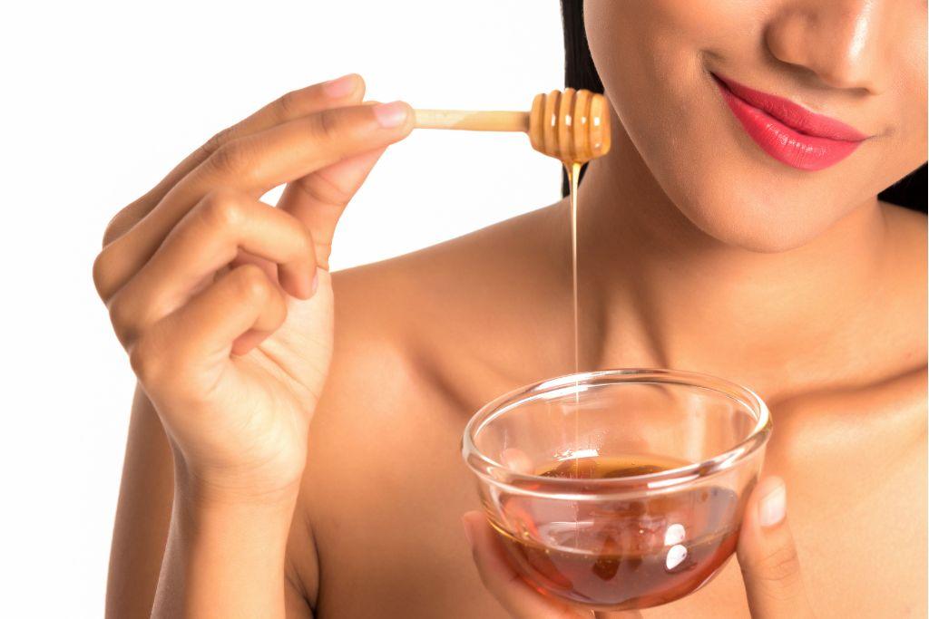 Woman applying honey for natural skincare with a bowl and honey dipper