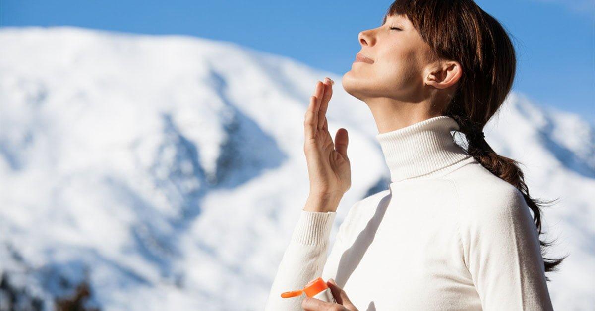 Woman applying skincare cream outdoors in snowy mountains, winter skin protection