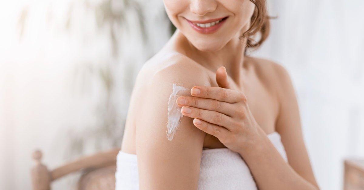 Woman applying natural skincare cream to shoulder, healthy glowing skin care routine